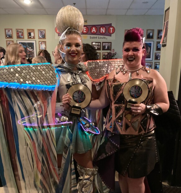 Katie Hepting and Sarah Bundy holding up their awards for their teams dressed in their Unravel outfits